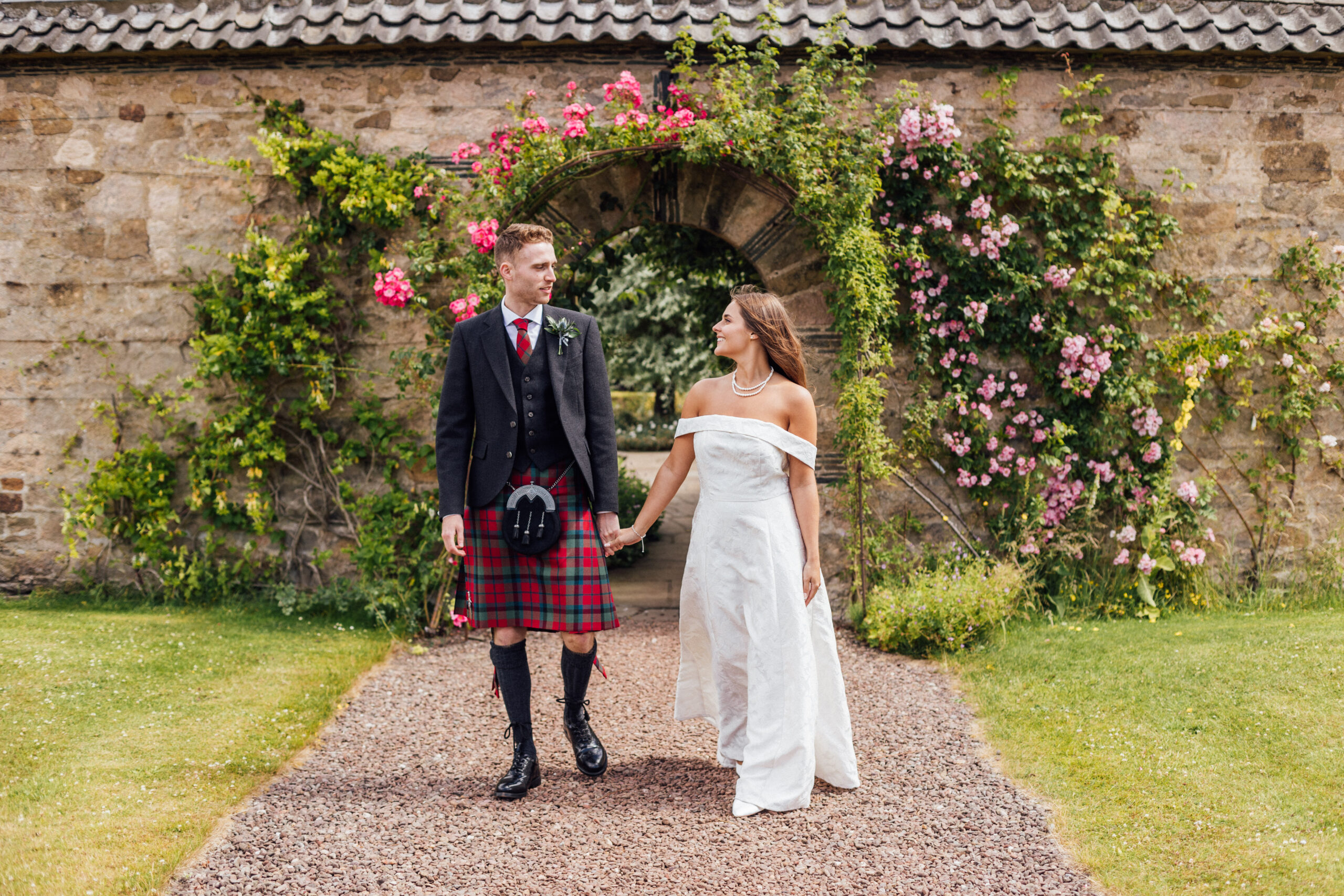 A bride and groom walk through a rose garden